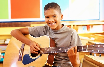 child with a smile holding a 
    	guitar